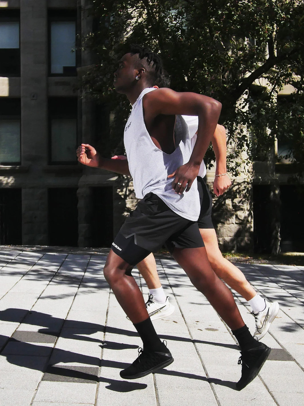 Two runners in an urban setting; one is wearing the 800m thigh phone holder under running shorts