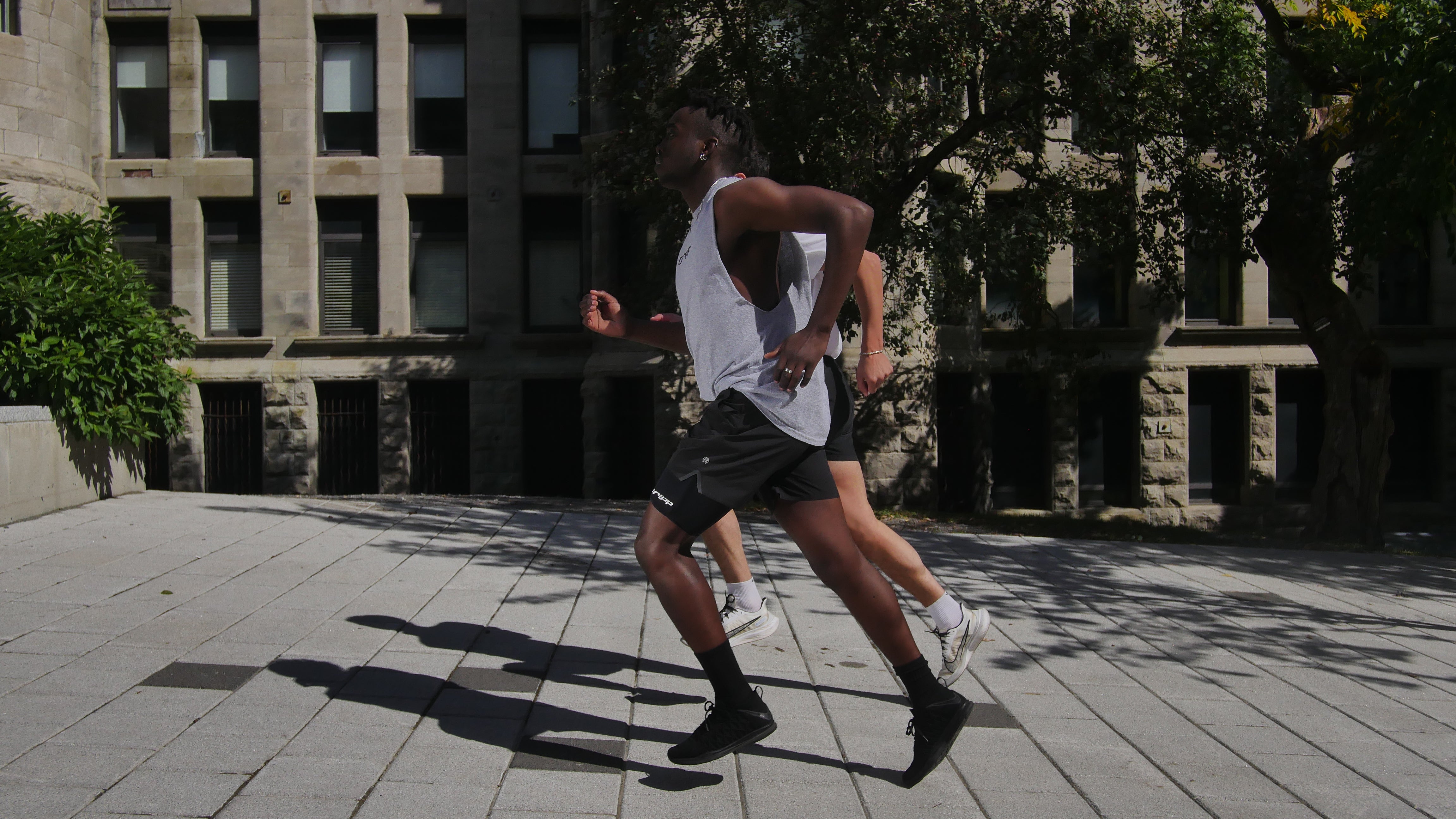 A full body picture of two people running in an urban area. One can clearly be seen wearing the legband sold by 800m.